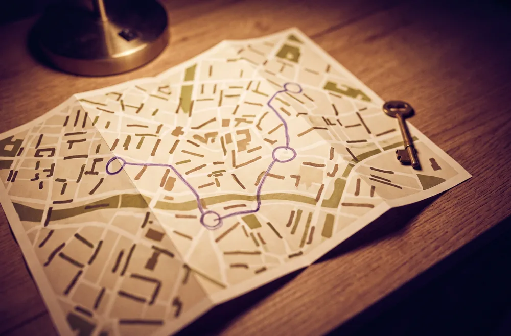 A folded cream city map with a violet ink route connecting three circled stops, a brass key beside it.